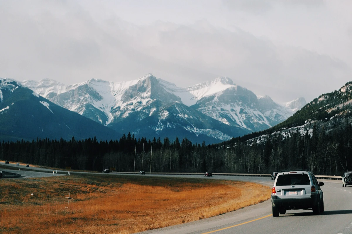 SUV on a highway below snow-capped mountains